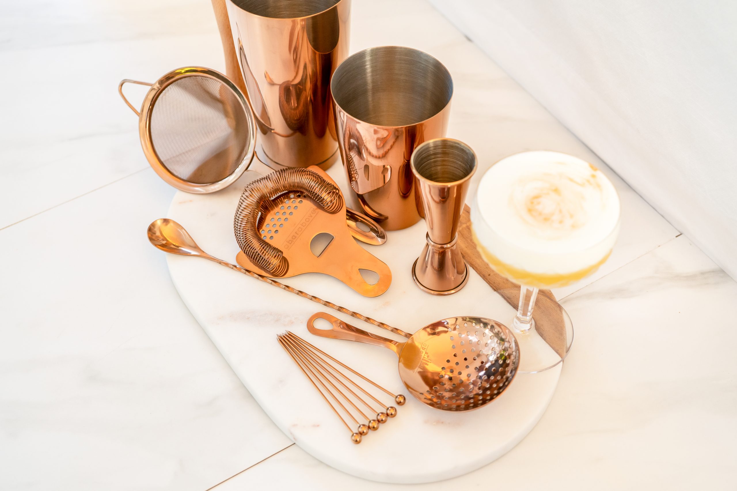 Shop Kitchen Cliques -Shop Kitchen Cliques bronze gift set of cocktail shaker strainer Hawthorn strainer set cocktail spoon for drink mixing and japanese jigger bronze next to an alcoholic drink concoction scaled 1